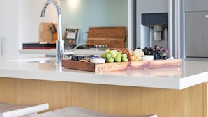 A kitchen counter with a wooden cutting board holding grapes and cheese, a sink, and a stainless steel faucet. - ZEN Paradise - 2-br Waterfront Ocean View Retreat (Darwin)