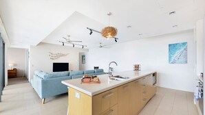 A modern kitchen with a central island, a built-in oven, and a dining area with a blue sofa. - ZEN Paradise - 2-br Waterfront Ocean View Retreat (Darwin)