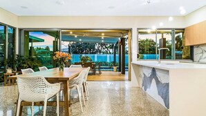 A modern dining area with a wooden table and white chairs, a kitchen counter, and a view of the outdoors. - Fred s at Fannie Bay - NT (Fannie Bay)