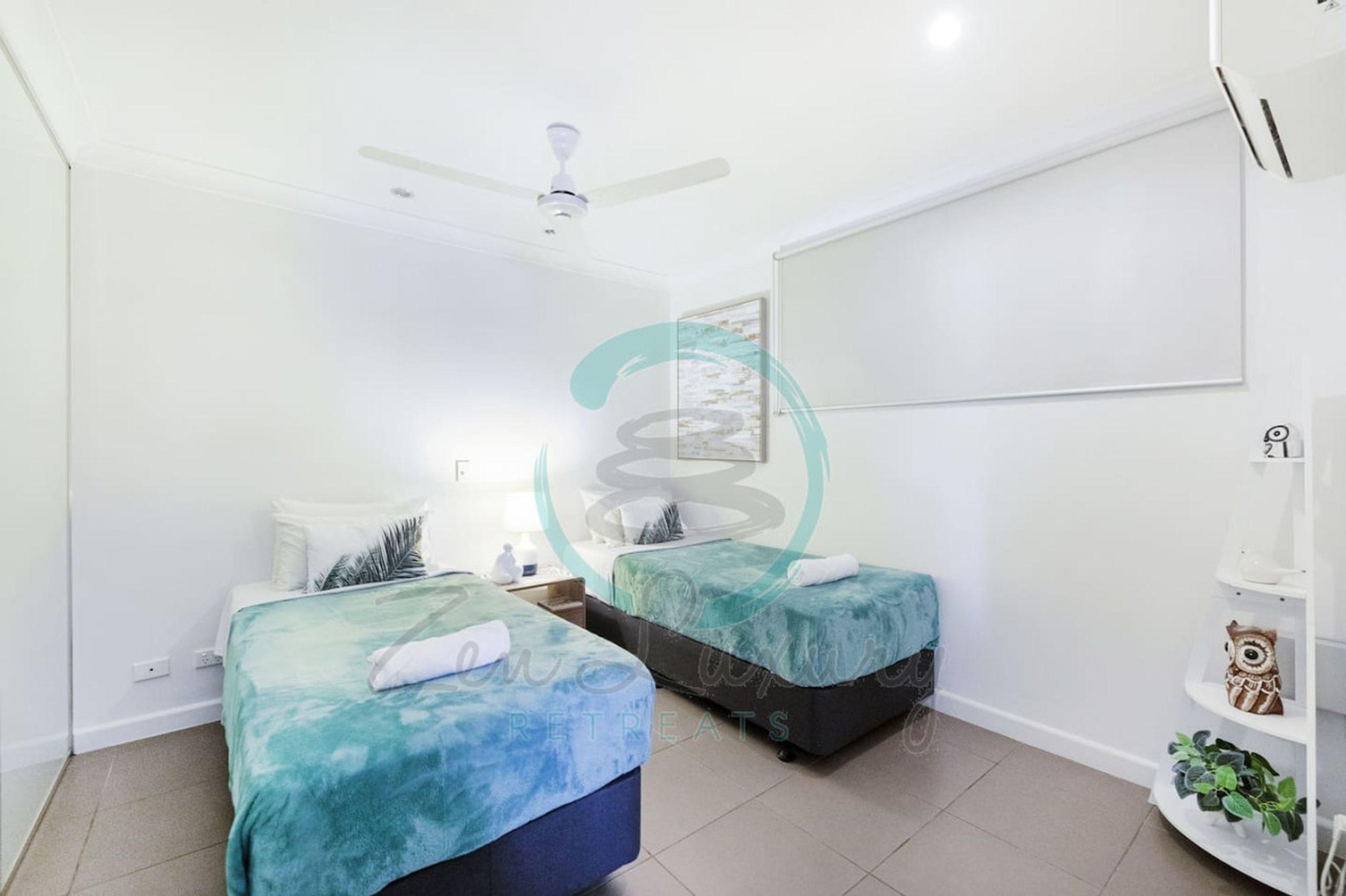 A room with two beds, a ceiling fan, a wall-mounted TV, and a small shelf with decorative items.