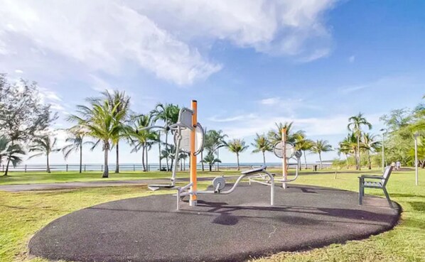 An outdoor exercise area with fitness equipment, surrounded by palm trees and a clear sky. - Zen Nomad Balcony Outdoor Dining Markets (Nightcliff)