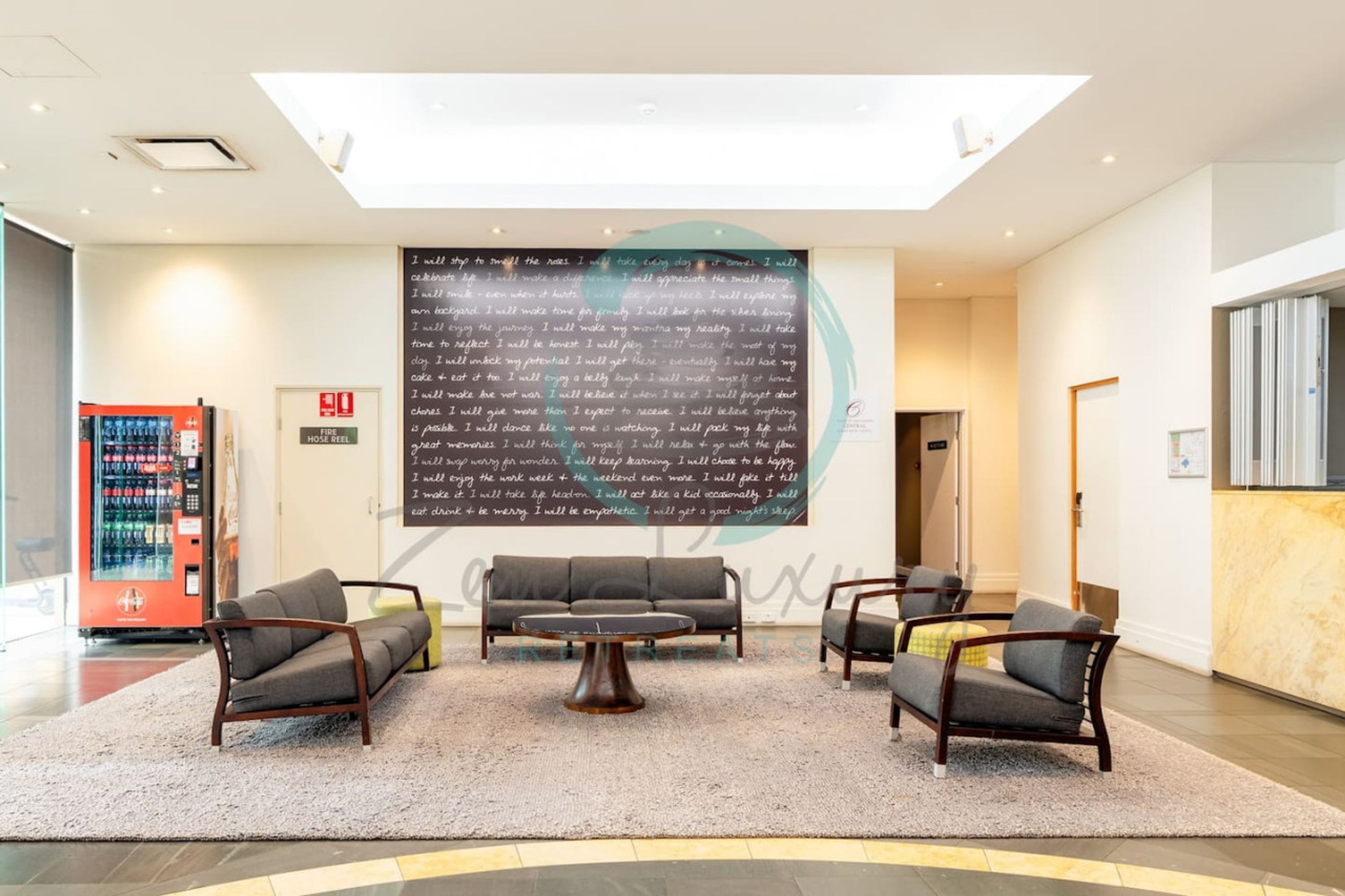 En moderne lobby med en stor tavle, der viser en liste over personlige mål, en rød brandalarm og en automat.
