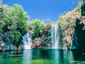 Ein Wasserfall mit klarem Wasser, das über Felsen fließt, umgeben von üppiger Vegetation.