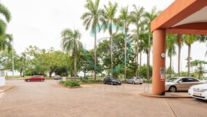 Un espace de stationnement où sont garées plusieurs voitures, avec des palmiers et un bâtiment sur lequel on peut lire une enseigne indiquant « RETRAITES ».