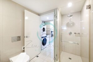 A modern bathroom with a glass-enclosed shower, a toilet, and a washing machine visible through an open door. - Reef-side Splendor City Vistas Pool Workspace (Darwin)