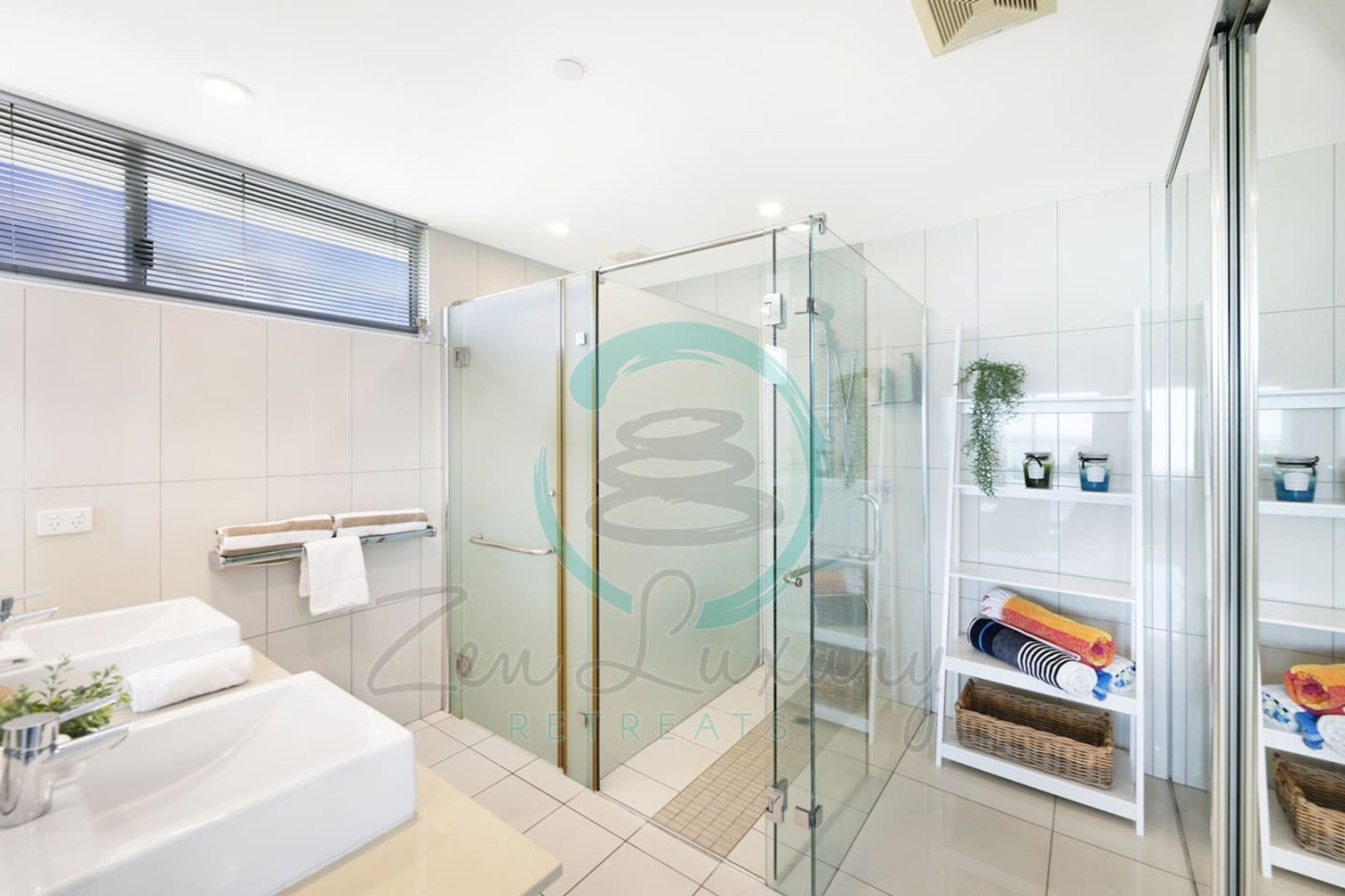 A modern bathroom with a glass shower enclosure, a white sink, and a shelf with towels and toiletries.