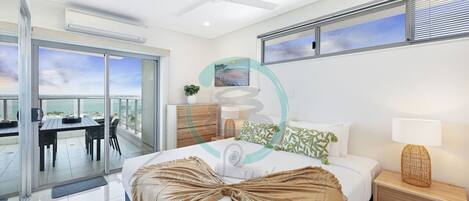 A modern bedroom with a bed, bedside table, and a view of the sea through large windows.