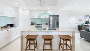 A modern kitchen with white cabinets, a central island with stools, and a refrigerator. - Zen Seabreeze Workdesk Balcony Dining Seaview (Darwin)