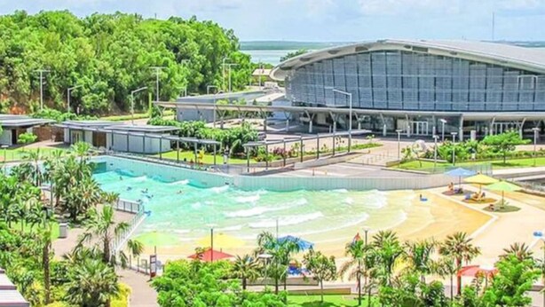 A large swimming pool with a beach area, surrounded by palm trees and a modern building with a curved roof. - Zen Ocean Meadows Sea View - Pool - Outdoor Dining (Darwin)