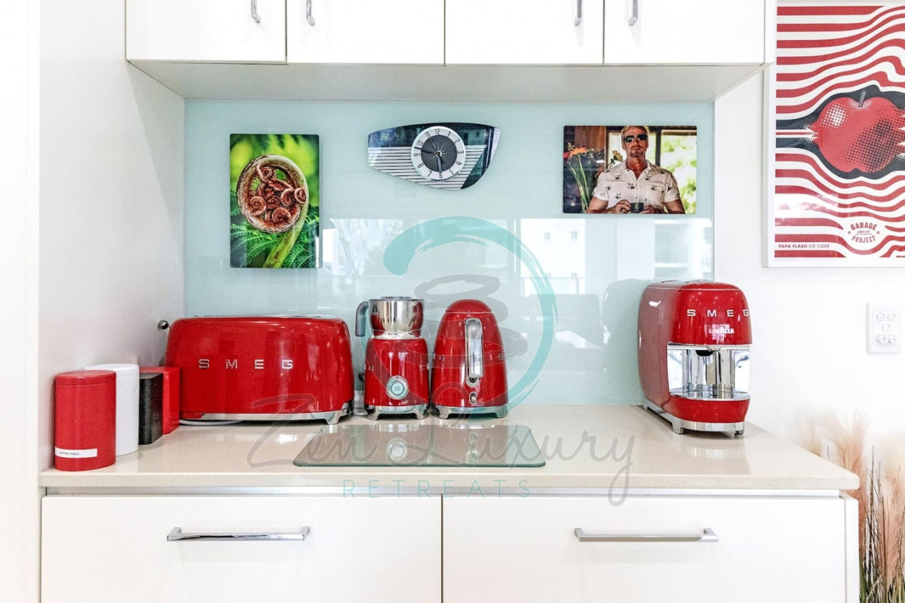 A kitchen with a white countertop, red appliances, and wall art including a clock and framed photos.