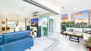 Uma sala de estar moderna com um sofá azul, uma mesa de centro de madeira e uma varanda com vista para a cidade.