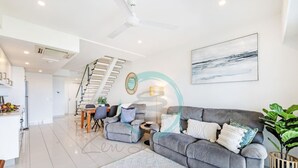A modern living room with a grey sofa, a coffee table, and a dining area with chairs and a table. - Seaview Haven Ocean Vistas Gym Pool Parking (Darwin)