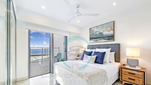 A modern bedroom with a bed, nightstand, and a painting of the sea. - Seaview Haven Ocean Vistas Gym Pool Parking (Darwin)