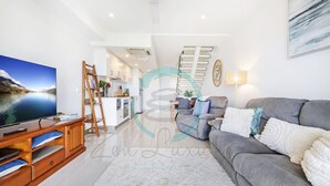 A modern living room with a grey sofa, a flat-screen TV, wooden entertainment unit, and a staircase leading to an upper level. - Seaview Haven Ocean Vistas Gym Pool Parking (Darwin)