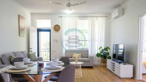 Ein modernes Wohnzimmer mit einer Couch, einem Esstisch, Stühlen, einem Fernseher und einer Pflanze.