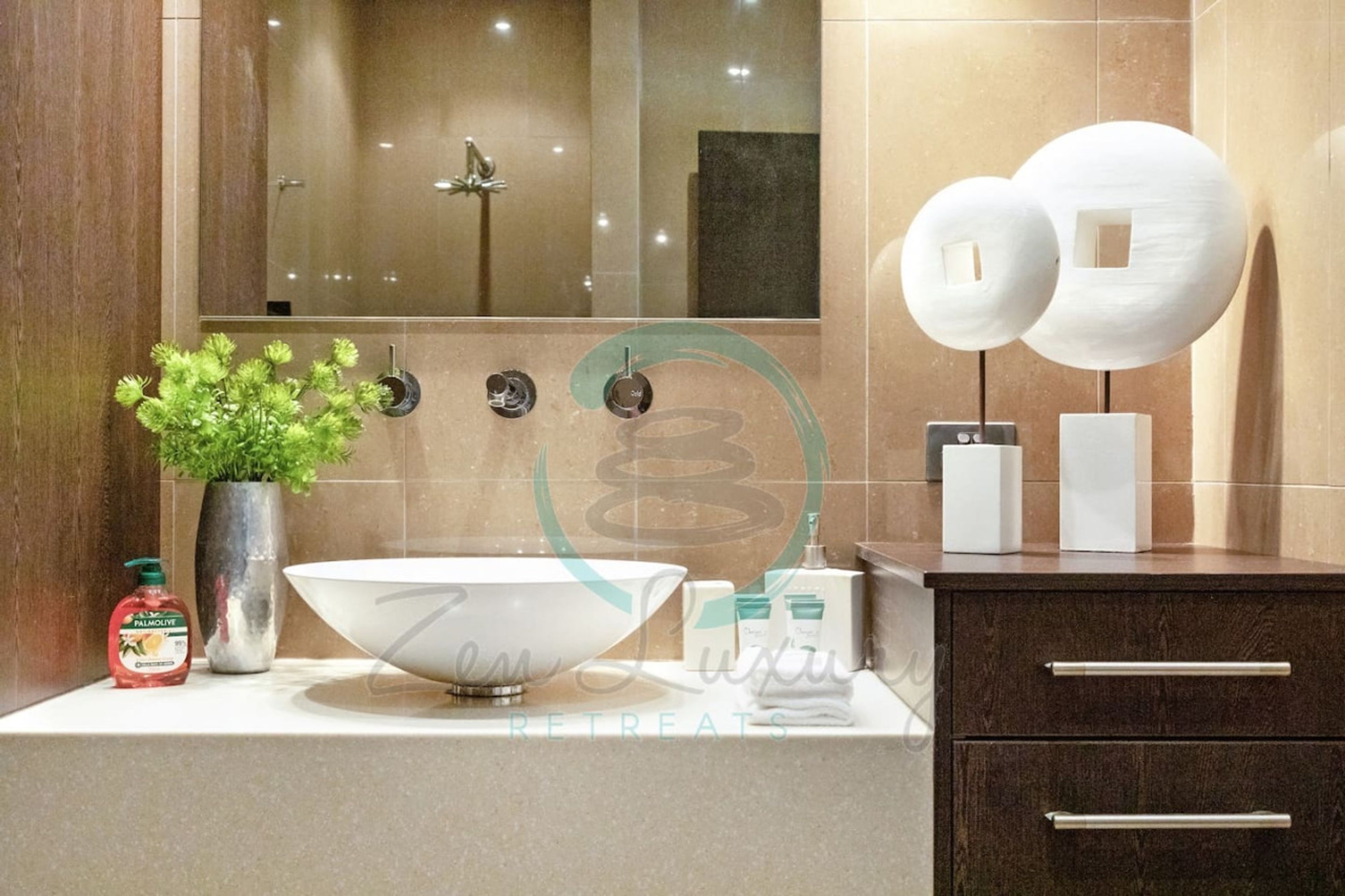 A modern bathroom with a large mirror, a bowl sink, a potted plant, and a dark wooden cabinet.