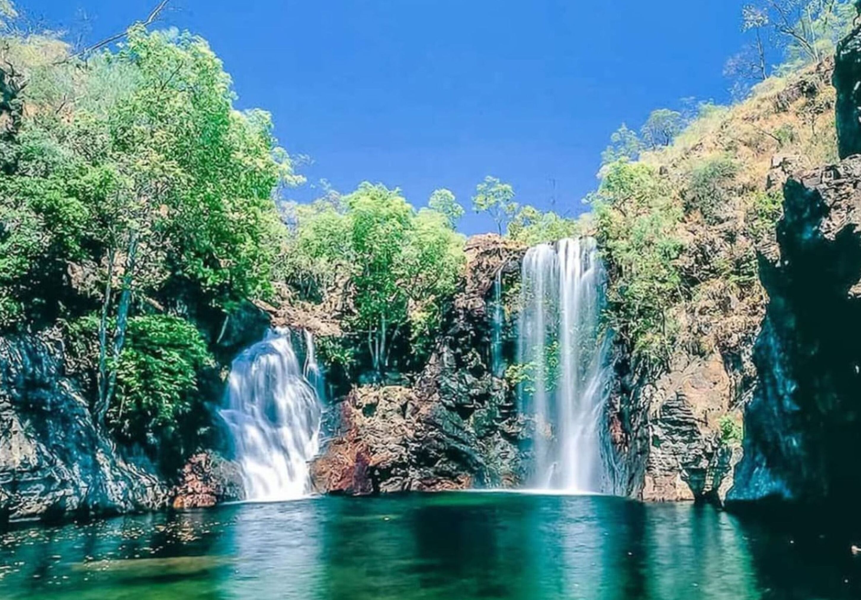 A waterfall cascading into a clear pool surrounded by lush greenery and rocky cliffs.