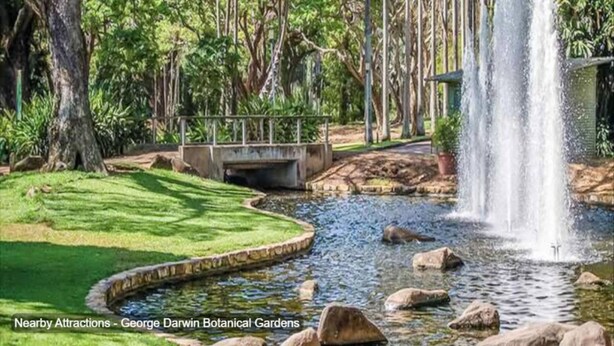 Un jardín tranquilo con cascada, puente y estanque rodeado de abundante vegetación.