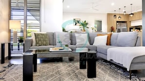 A modern living room with a grey sectional sofa, a glass coffee table, and a patterned rug. - Zenhouse Vista Elegant Coastal Haven (Muirhead)