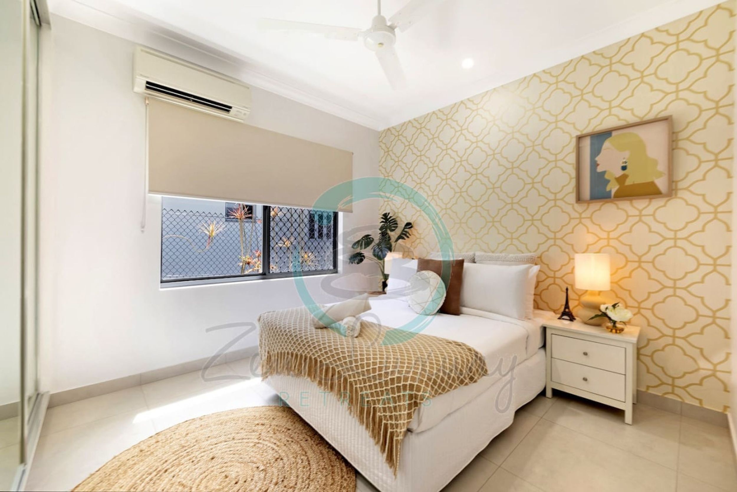 A bedroom with a bed, bedside table, lamp, and a window with a view.