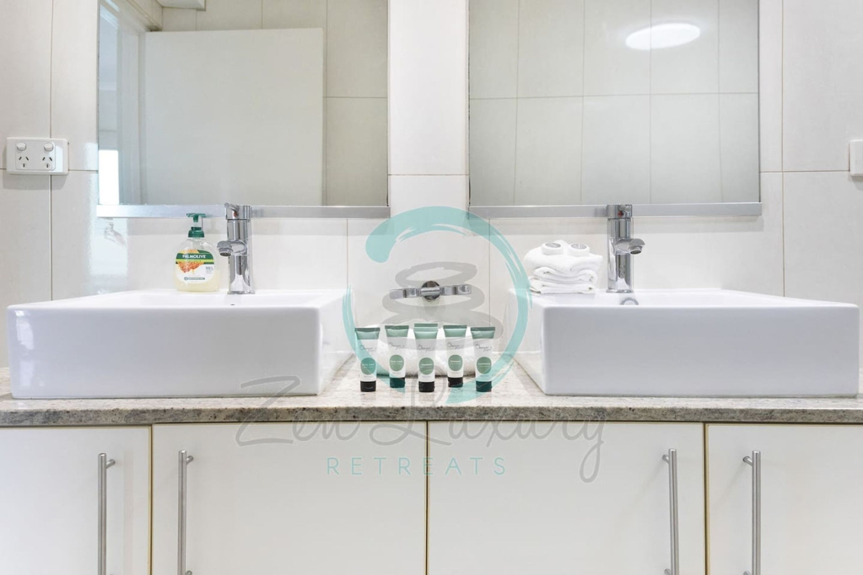 A bathroom with two sinks, a mirror, and toiletries on the countertop.