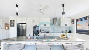 A modern kitchen with a central island, bar stools, stainless steel appliances, and a view of the city. - Pinnacle Penthouse Ambience Views Pool Gym (Darwin)