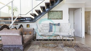 A modern living room with a staircase, a white sofa, two armchairs, and a glass coffee table. - Pinnacle Penthouse Ambience Views Pool Gym (Darwin)