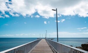 A wooden pier extending into the sea with railings on both sides and street lamps. - Lux Beachfront PH Office Pool Skyline Views (Woolner)