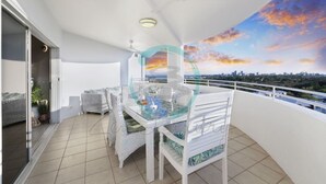 Ein Balkon mit Glastisch und Stühlen, einem Deckenventilator und Blick auf die Stadt.