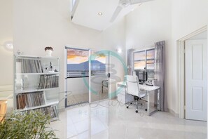 A modern room with a glass wall, a desk, and a bookshelf. - Lux Beachfront PH Office Pool Skyline Views (Woolner)