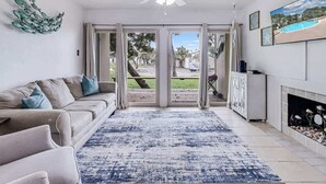 A living room with a sofa, a ceiling fan, a fireplace, and a view through glass doors. - Adventure House #17 (Rockport)