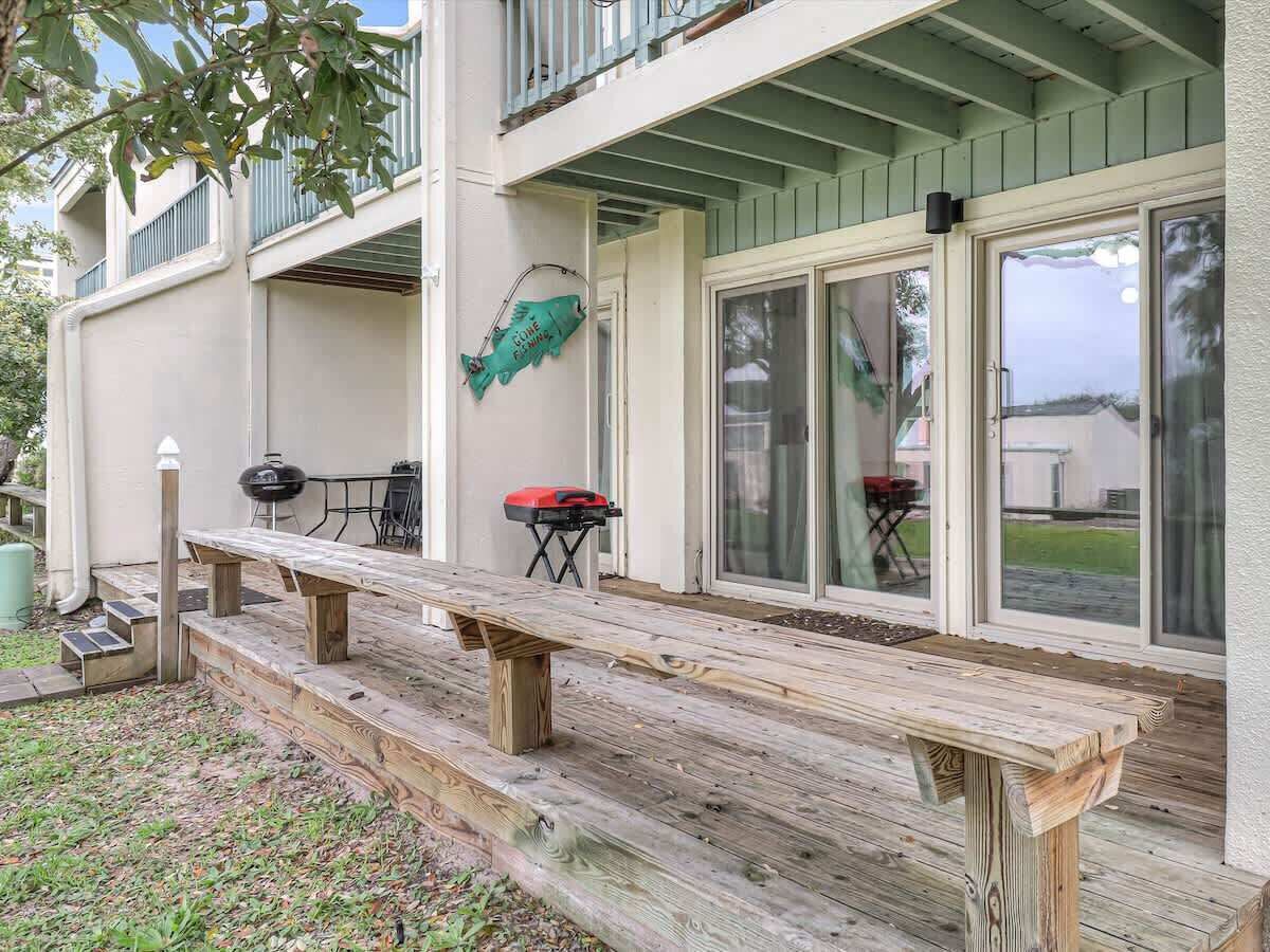 A wooden deck with a grill and a table, a covered patio area, and a view of the surrounding neighborhood.