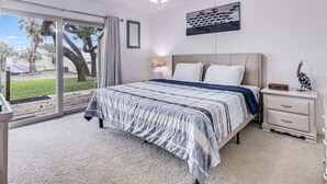 A bedroom with a bed, a ceiling fan, a nightstand, a lamp, and a view of the outdoors. - Adventure House #17 (Rockport)