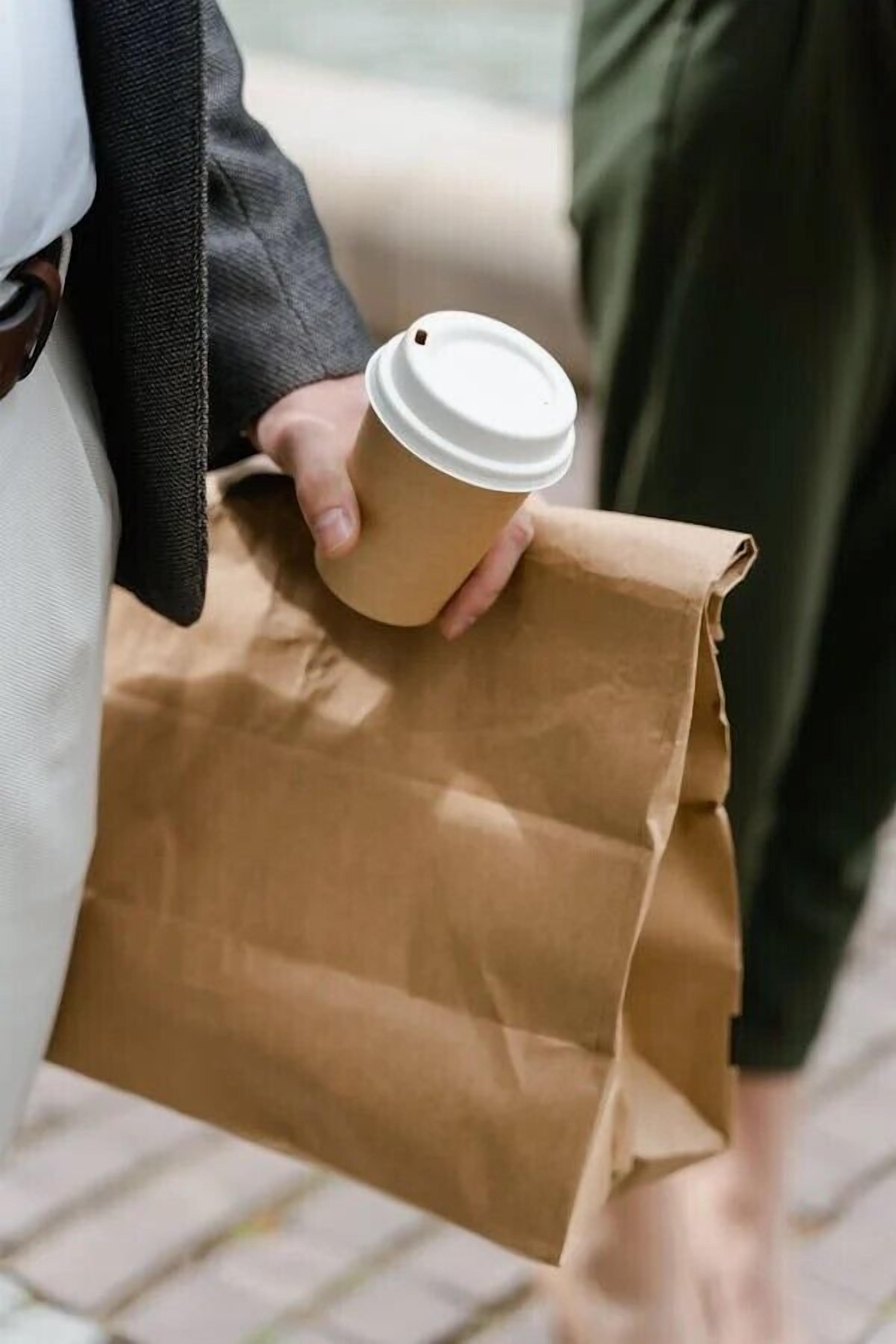 Une personne tenant un sac en papier et une tasse de café.