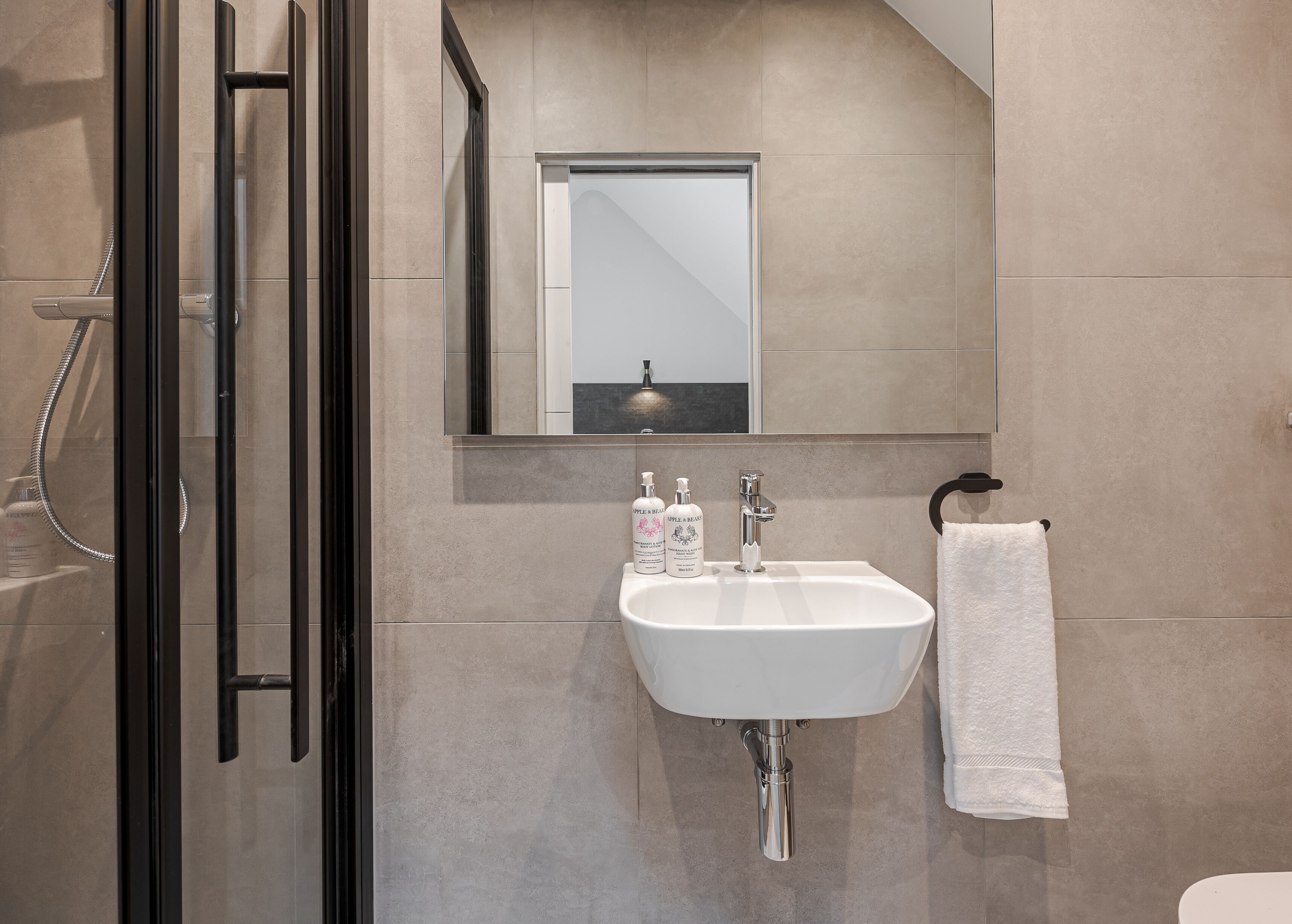A modern bathroom with a glass shower enclosure, a white sink with a mirror above it, and a towel hanging on a rack.