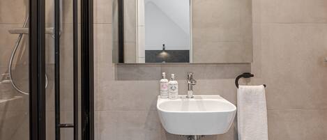 A modern bathroom with a glass shower enclosure, a white sink with a mirror above it, and a towel hanging on a rack.
