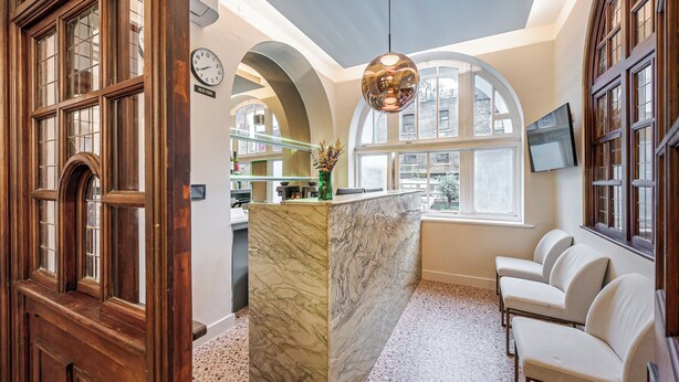A hotel lobby with a marble reception desk, seating area, large windows, and a clock on the wall. - King's Cross Express Inn (London)