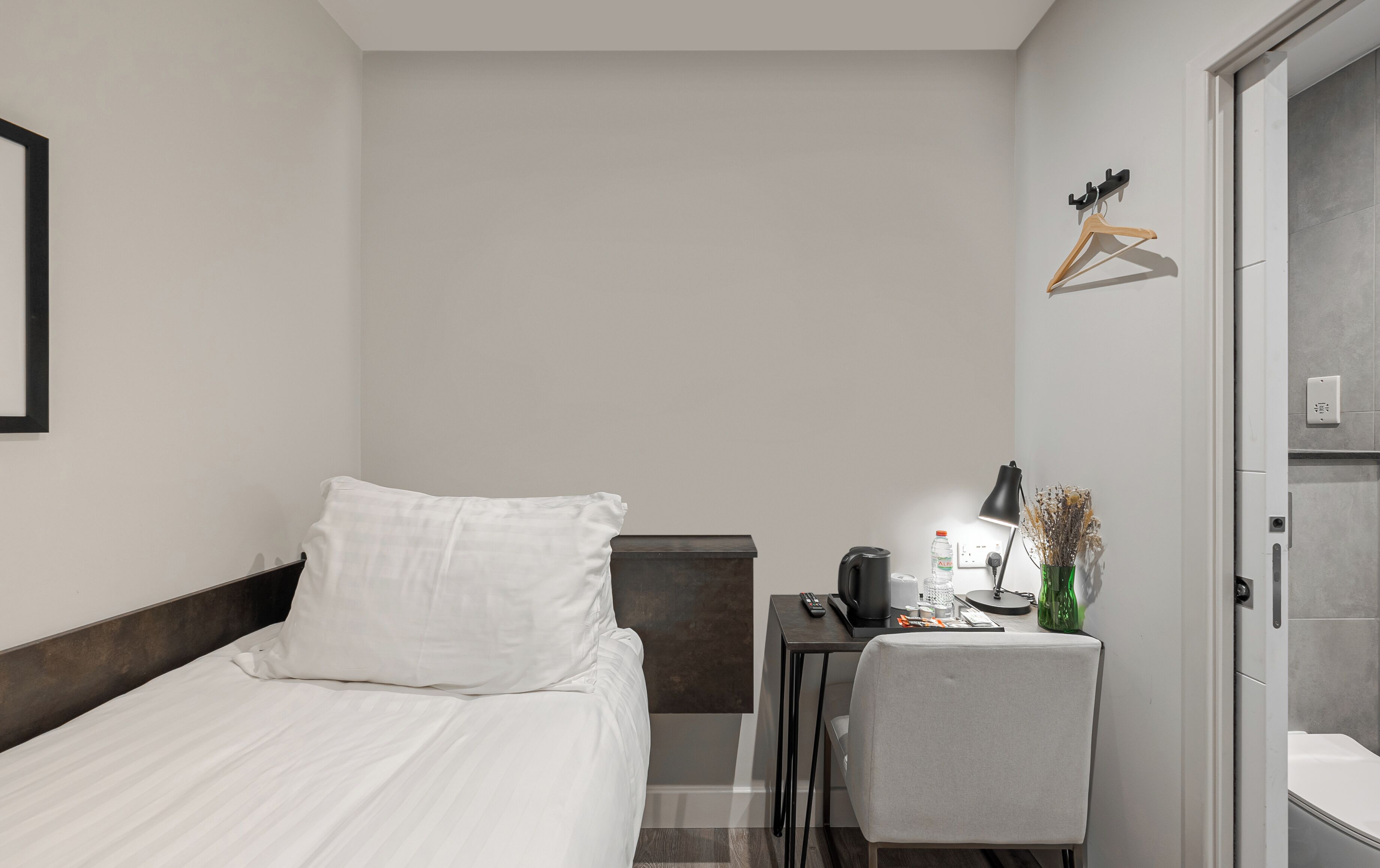 Quarto de hotel com cama, escrivaninha com luminária, cadeira e guarda-roupa.