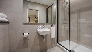 A modern bathroom with a glass-enclosed shower, a sink with a mirror above it, and a toilet. - King's Cross Express Inn (London)