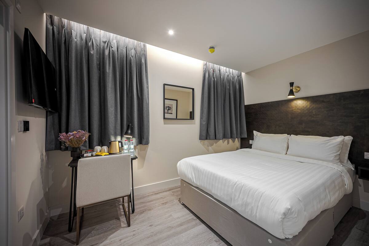Une chambre d’hôtel moderne équipée d’un lit, d’un bureau, d’une chaise, d’un téléviseur à écran plat et d’une table de chevet avec une lampe et des articles de toilette.