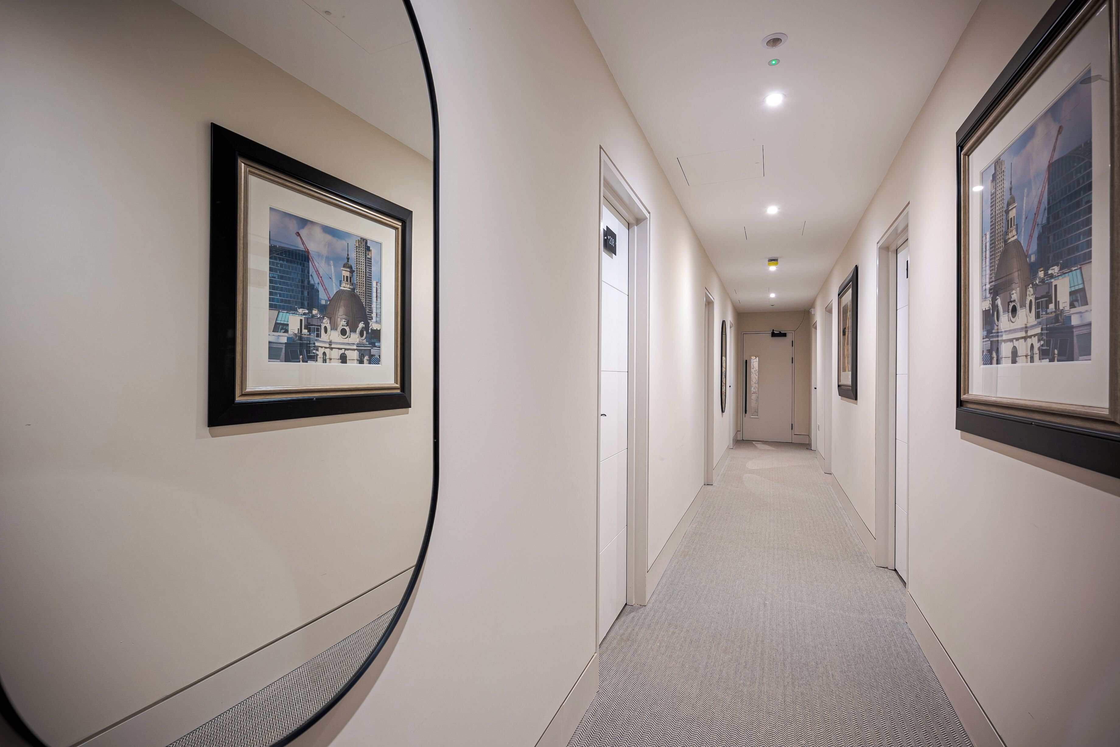 A hallway with framed pictures on the walls, doors leading to rooms, and a carpeted floor.