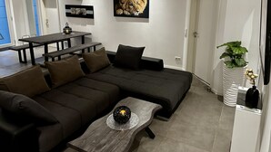 Un salon moderne avec un canapé d’angle, une table basse en bois, une table à manger avec des bancs et un grand tableau encadré représentant un lion.