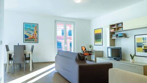 Una sala de estar moderna con un sofá, una televisión, una estantería y un comedor con sillas y una mesa.