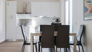 Una cocina moderna con armarios blancos, una campana extractora de acero inoxidable y una zona de comedor con una mesa de madera y cuatro sillas.