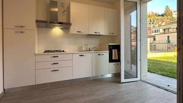 Una cocina moderna con armarios blancos, una campana extractora de acero inoxidable y un puerta corrediza de vidrio que da a un balcón.