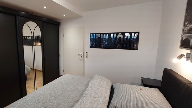 Ein Schlafzimmer mit Bett, Kleiderschrank, einer Tür und einem Wandbild.