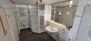 Ett badrum med en dusch som är avskärmad med glasväggar, ett vitt handfat och en stor spegel.