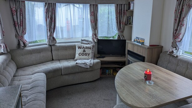 Una sala de estar acogedora con sofá, televisión, una mesa con vela y cortinas de estampado floral.