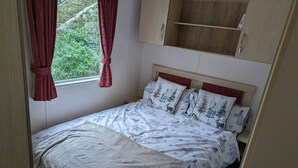 Un dormitorio con cama, almohadas, una ventana con cortinas y un armario de madera.