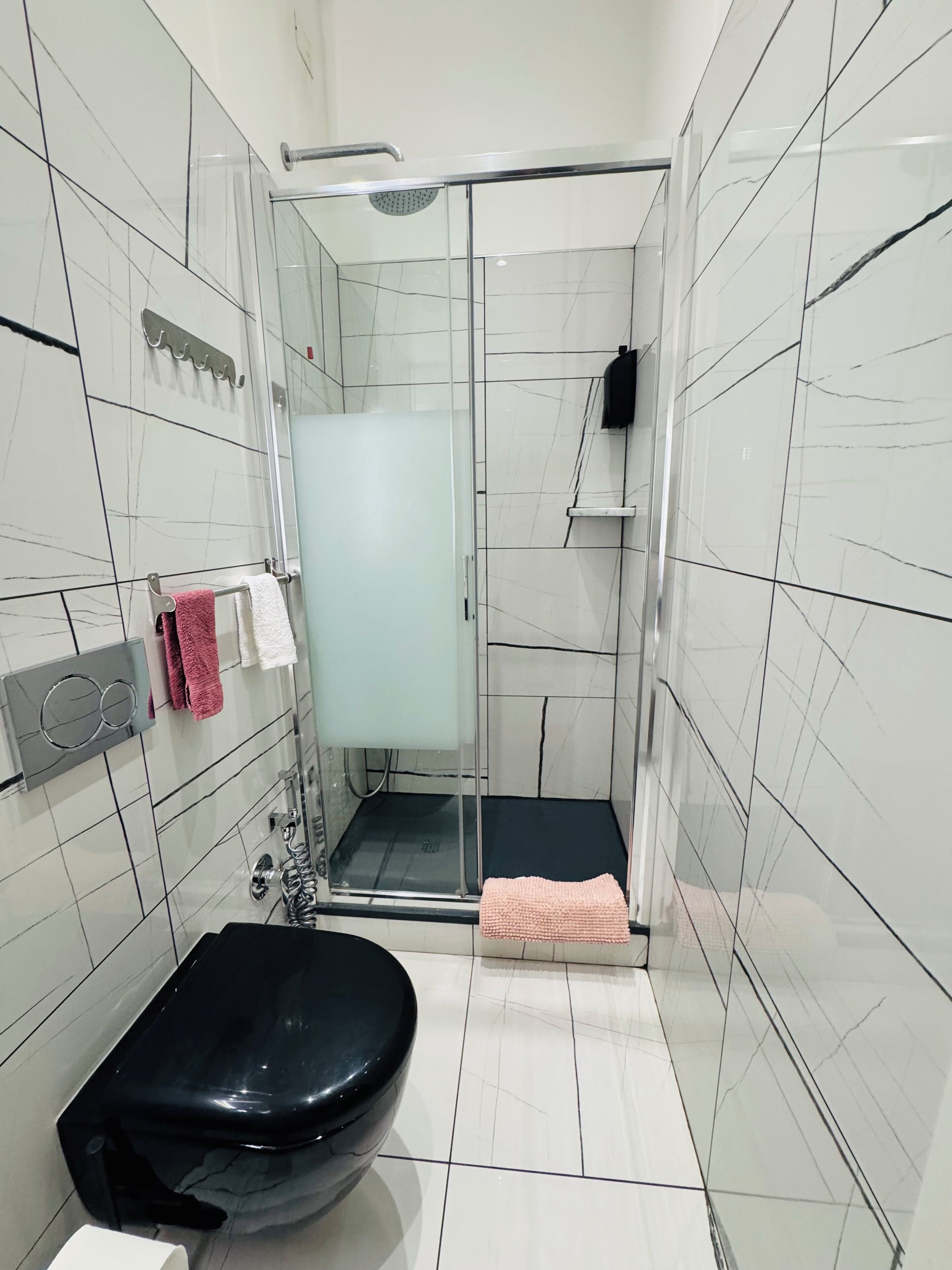 A bathroom with a glass-enclosed shower, a black toilet, and a white sink.